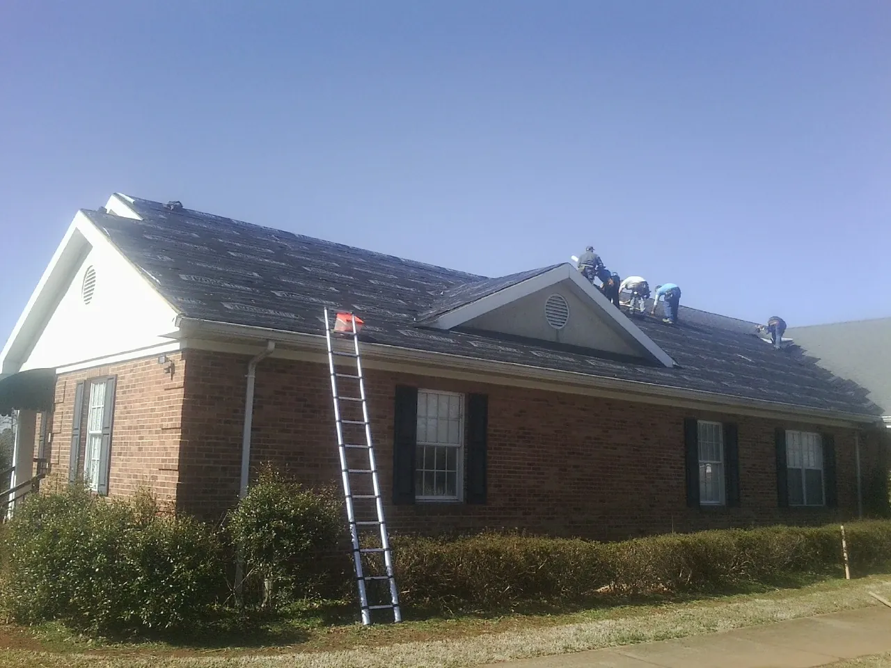 Crew tearing shingles off a brick ranch roof with a ladder set — Emergency Roof Repair work by our crew in Union Bridge