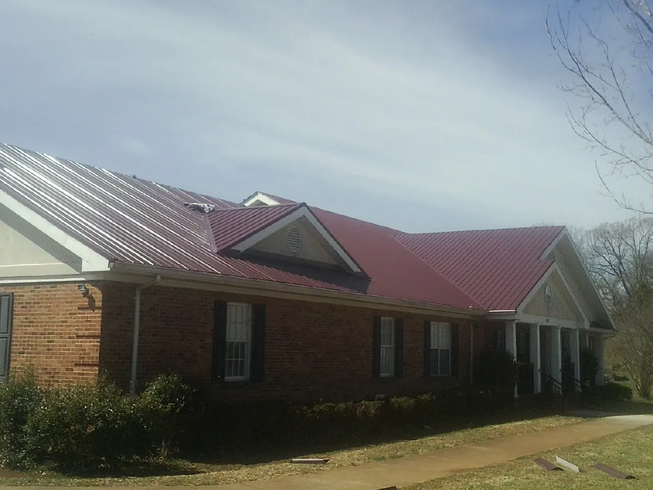 Red metal roof with gabled entries on a long brick building, from a Hail Damage Roof Repair job in Union Bridge
