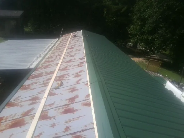 Old rusted panels beside newly installed green metal roofing — Wind Damage Roof Repair by Roofing Brothers in Union Bridge