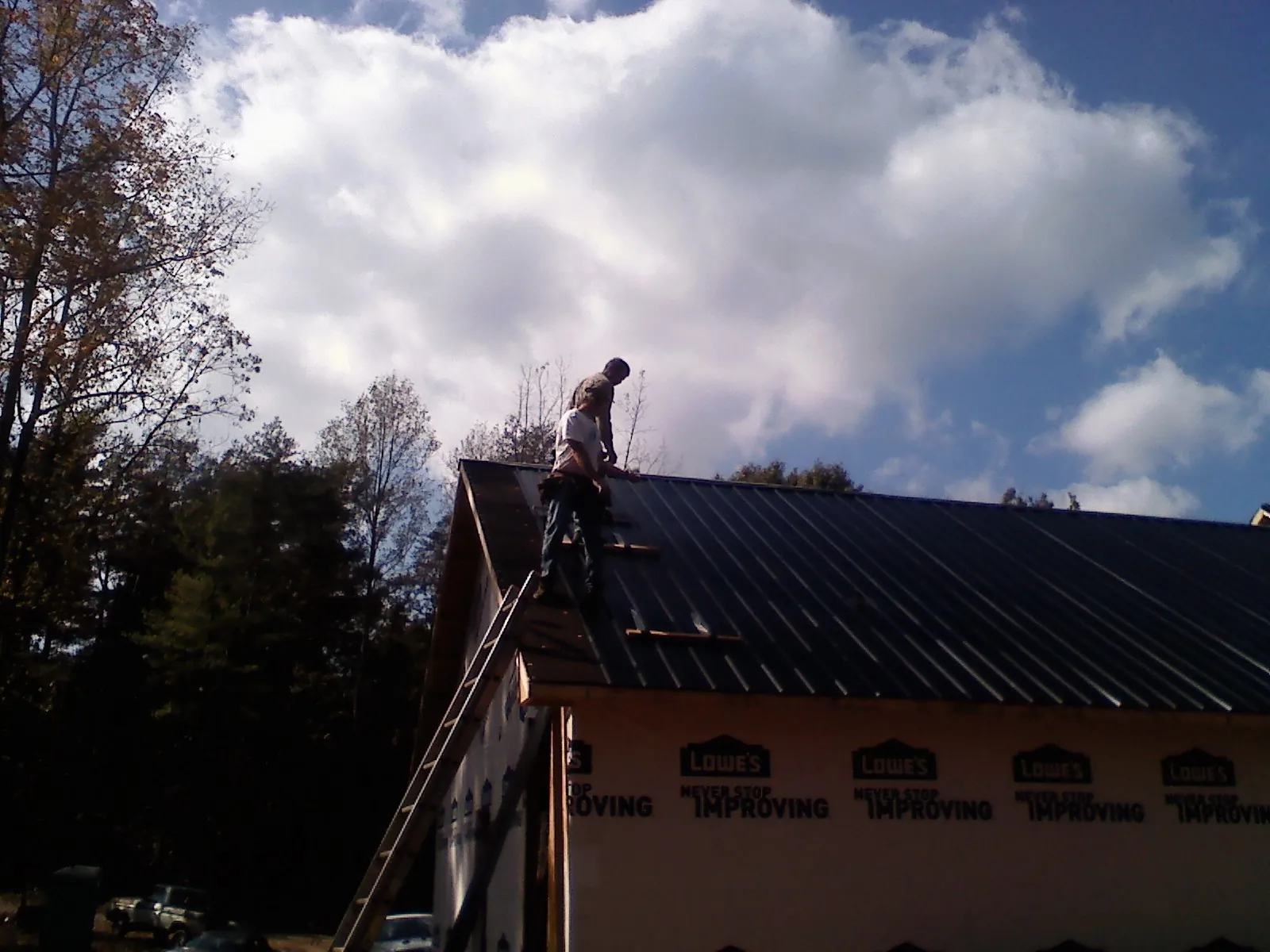 Roofer fastening dark metal panels high against a cloudy sky, from a Roof Inspection job in Union Bridge