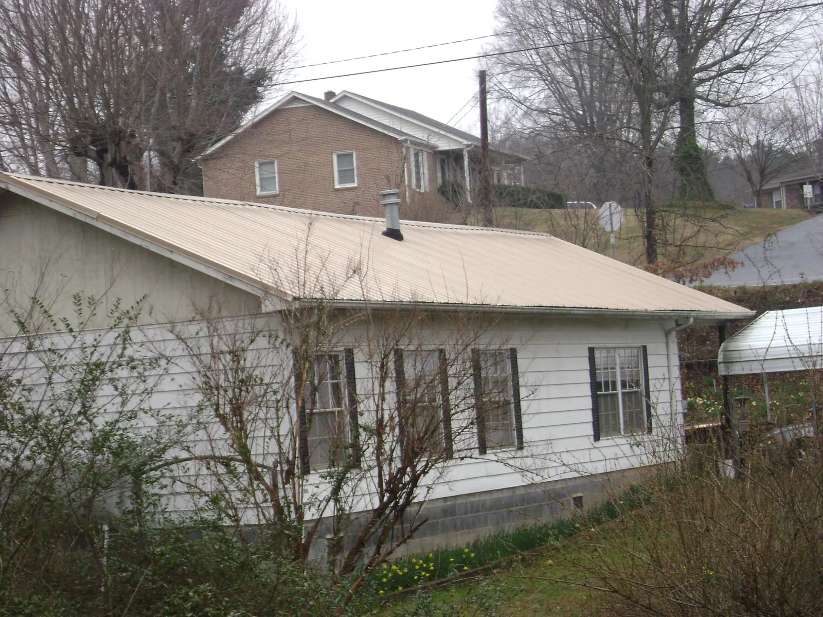 Tan metal roof on a white sided house set into a hillside — Commercial Roofing by Roofing Brothers in Union Bridge